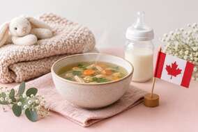 淡粉色桌面上的一碗雞湯、奶瓶、針織毯與加拿大小國旗